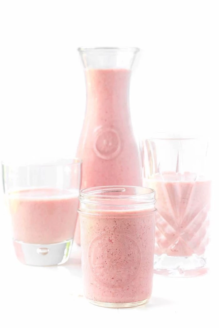 fruit smoothie recipes, simple pastel pink-colored strawberry smoothie, in pitcher and three glasses, on a pure white background
