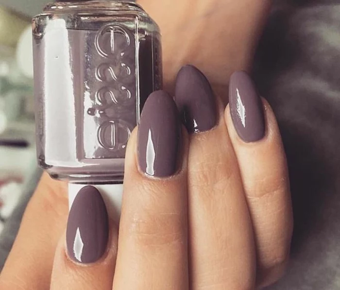 oval-shaped short stiletto nails, painted in plum colored nail polish, on hand holding nail polish bottle