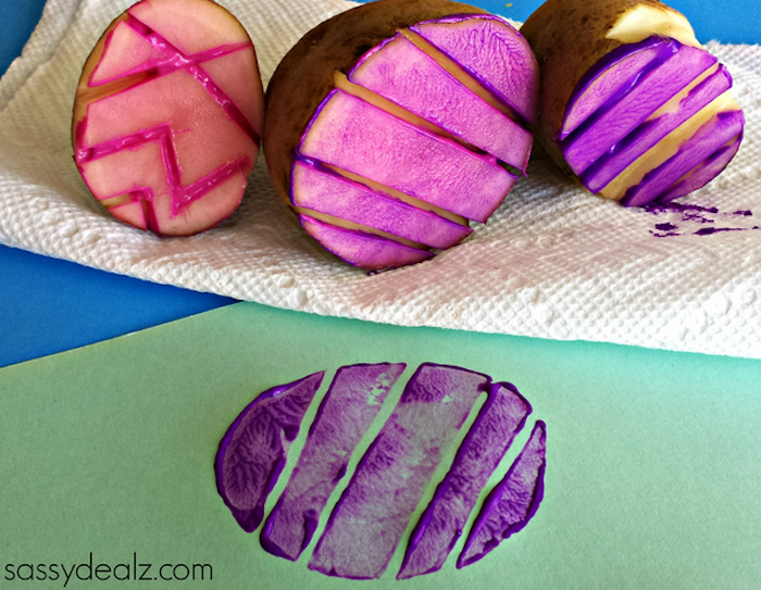 several stamps made from potatoes, shaped like easter eggs, with different carved patterns, easter crafts for preschoolers, covered in pink and purple paint, sheet of green paper with print nearby