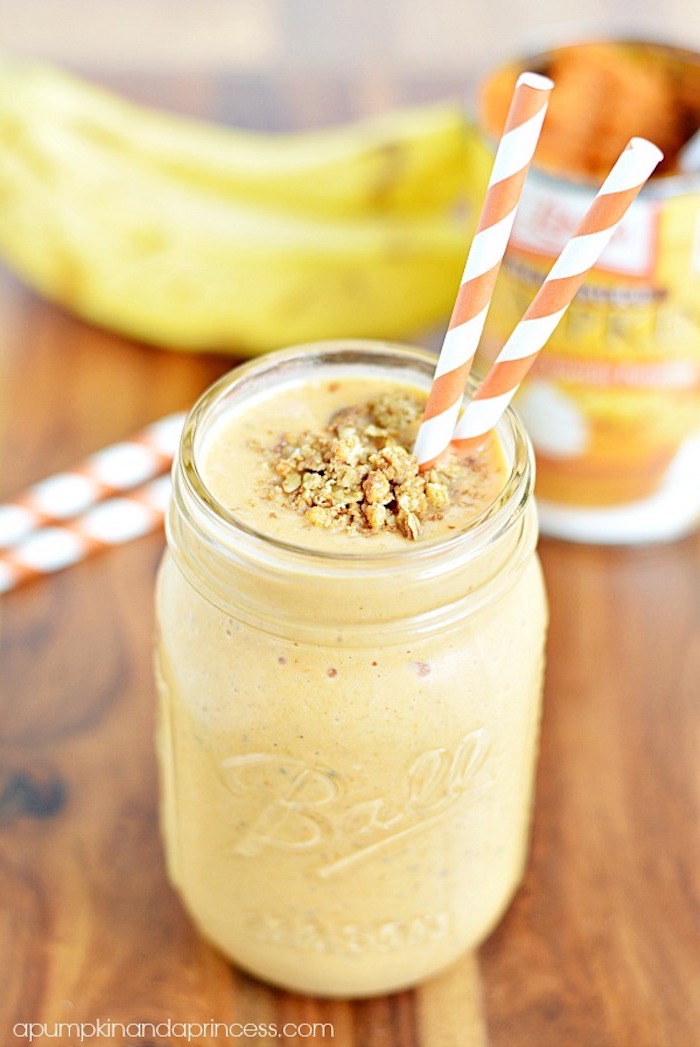 striped paper straws in white and orange, inside a ball jar, filled with creamy pale orange drink, topped with crushed nuts, easy smoothie recipes, bananas in background