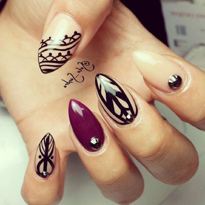 rhinestone gem-like stickers, in dark grey or black, on stiletto acrylic nails, painted in pale beige and purple, and decorated with black, hand-drawn designs