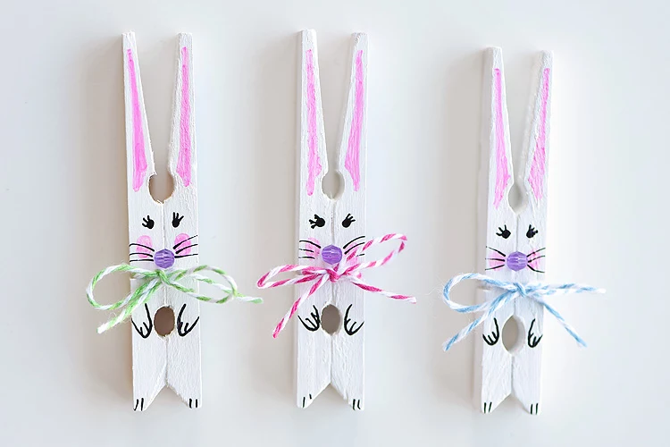 painted white clothespins, decorated to look like bunnies, easter crafts for adults, with bows made from two-tone thread