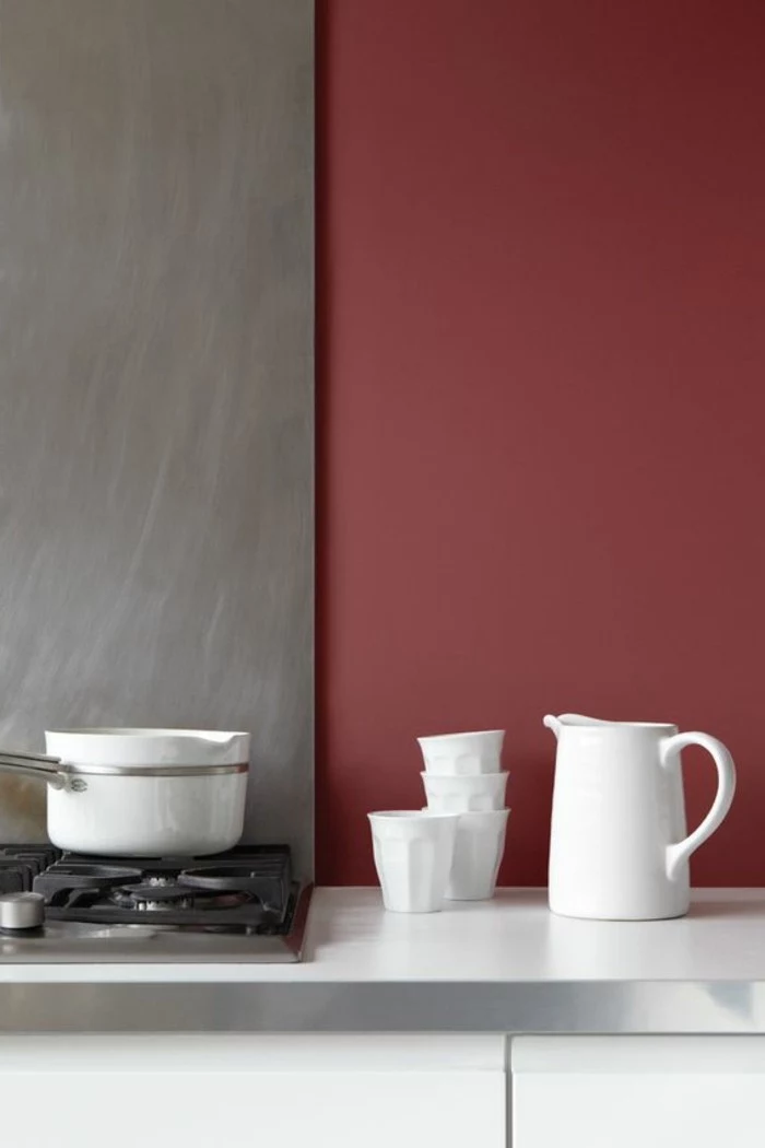 burgundy red and gray kitchen, with white cupboards and a stove, white jug with four matching ceramic cups, what color curtains with gray walls