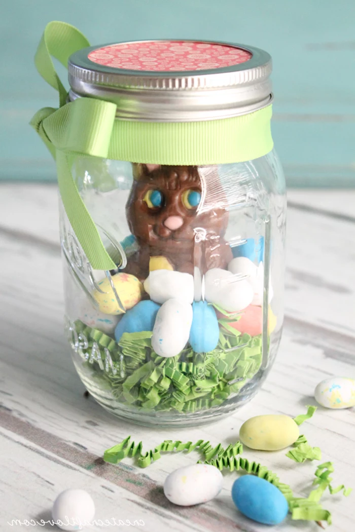 closed jar with pale green ribbon, tied in a bow, easter projects, containing pale green easter grass, multicolored egg-shaped candy, and a large chocolate bunny