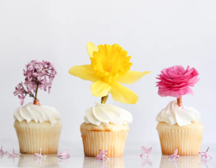 three cupcakes with white frosting, decorated with fresh flowers, lilac and daffodil, vibrant pink rose, mothers day gifts