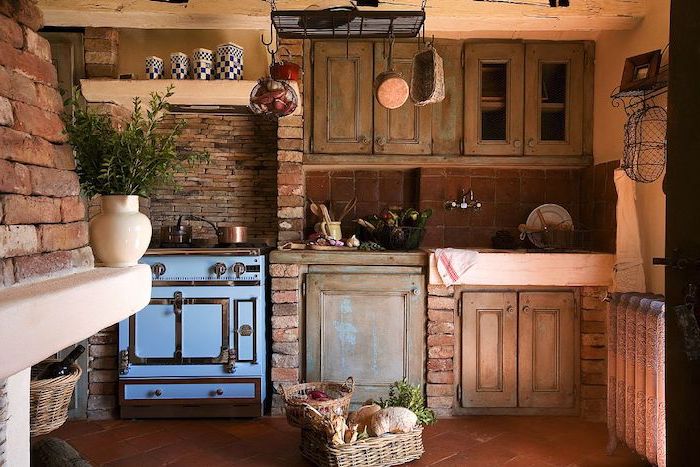 baskets with bread and other items, on a brown tiled floor, inside a kitchen with pale orange walls, and brick details, country kitchen decorating ideas, vintage wooden cupboards and an antique stove