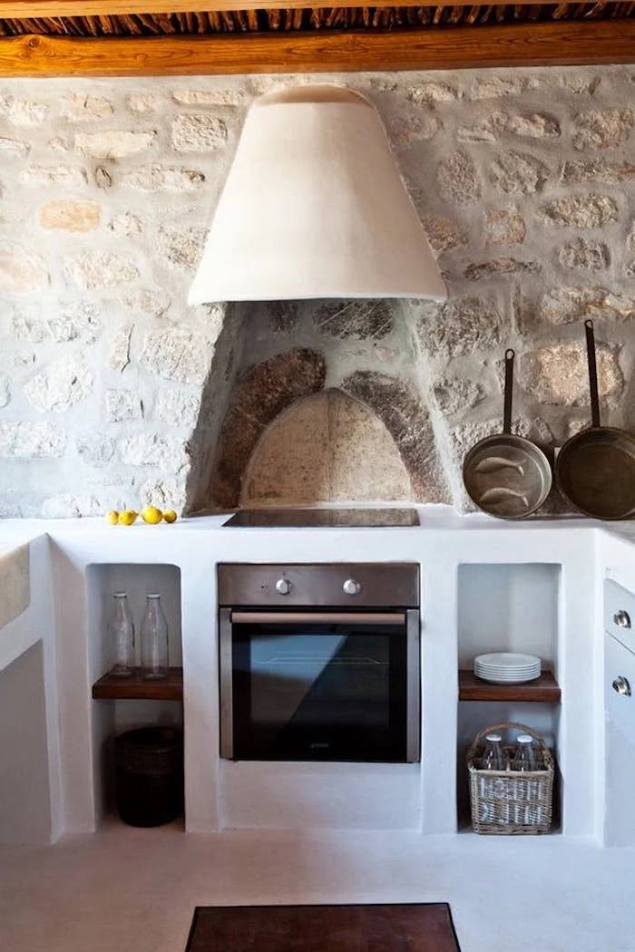 pans and bottles, in a kitchen with stone-covered walls, white lime plaster country kitchen cabinets, modern stove and wooden ceiling