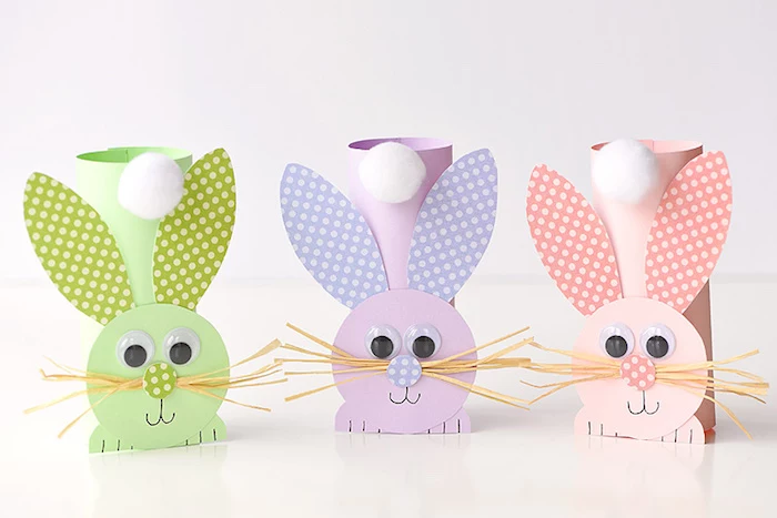 bunny ornaments, craft ideas for kids, made from pale green, pale purple and pale peach plain and patterned paper, decorated with eye stickers, faux straw whiskers, and cotton ball tails