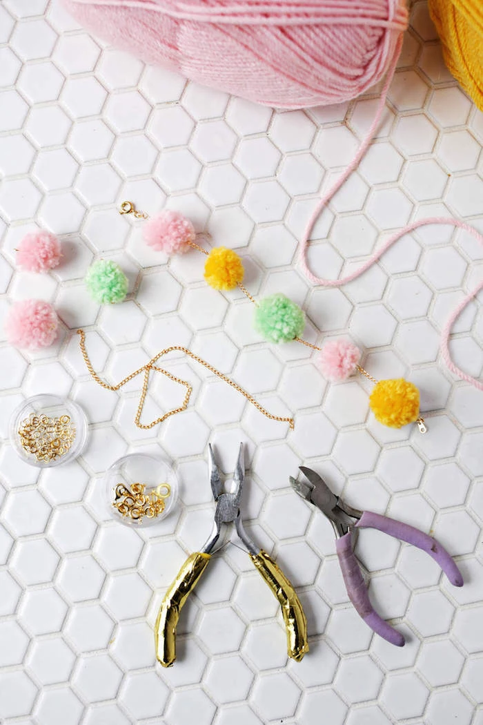 stringing pompoms together, on a thin golden chain, two pliers and jewelry making supplies, gift ideas for mom, pink and yellow woolen thread
