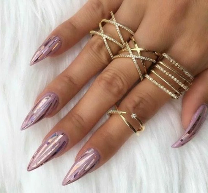 metallic-colored shards, on long stiletto nails, painted in rose ash pink nail polish, on hand with several rings