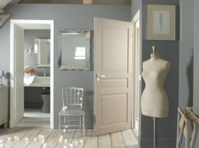 mirror and vintage chair, walls with blue grey paint, white door looking inside a bathroom, light wooden floor, fairy-lights and a dressmaker's dummy