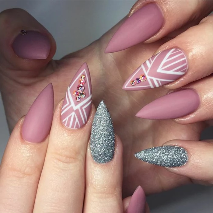 matte pink nail polish, with white decorations, and accent nails, covered in silver glitter, on two hands with long manicure, sharp stiletto nails