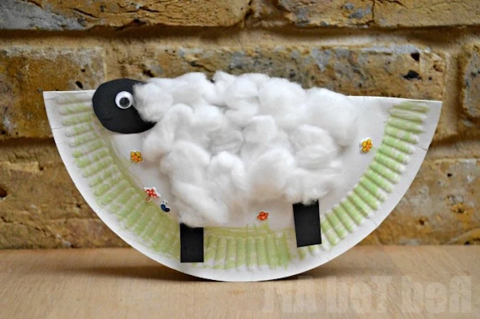 cotton covered collage of a sheep, with head and legs made from black paper, stuck on folded white paper plate, easter crafts for preschoolers, hand-drawn grass, and flower stickers
