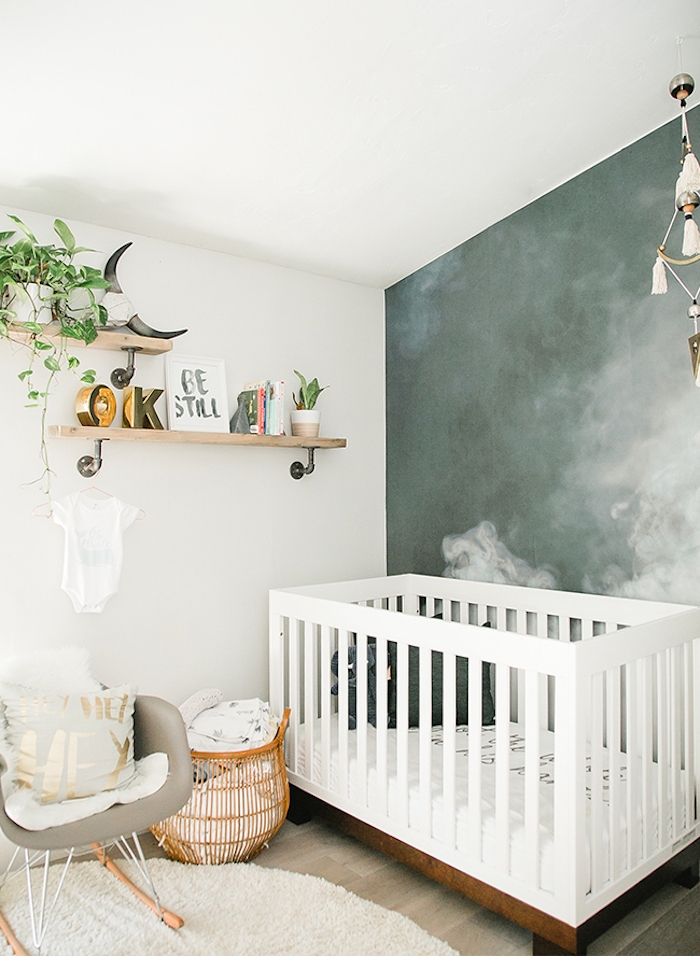 dark bluish-gray mural with white clouds, two wooden shelves, with potted plants, white wooden crib, and beige rocking chair, in gender neutral nursery