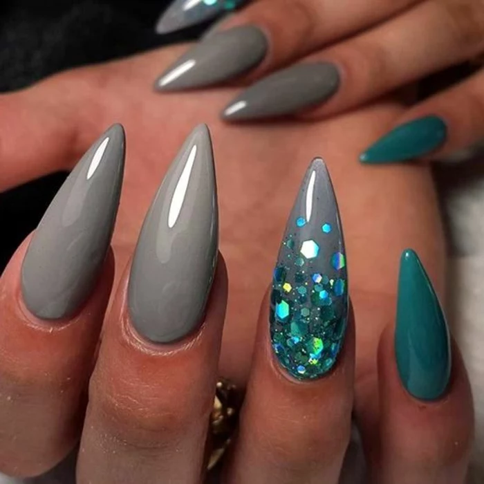 acrylic manicure covered with smooth, grey and turquoise nail polish, long and sharp stiletto nails, with iridescent light blue glitter