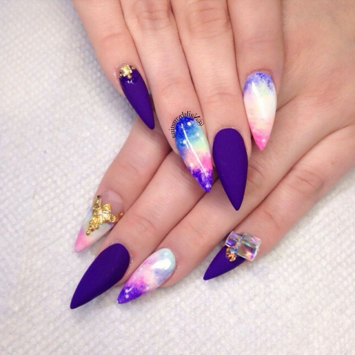 sunset sky-colored, long stiletto nails, with splashes of blue and pink, purple and white, matte purple manicure, decorative golden and iridescent stickers