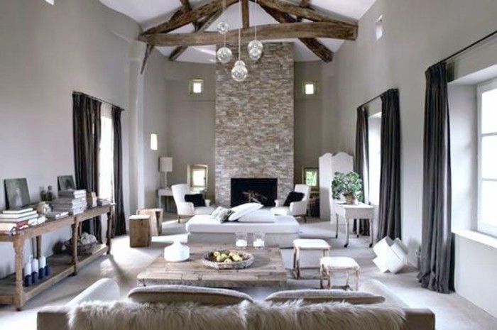 large living room, with big fireplace, wooden beams on ceiling, creamy pale grayish-brown walls, living room paint colors, wooden furniture and dark curtains 