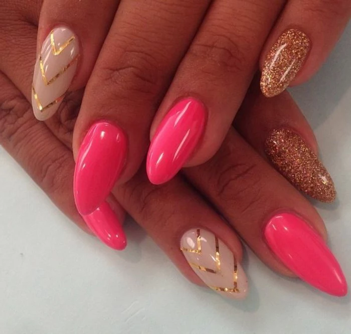 hot pink and beige nail polish, decorated with golden glitter and stripes, on oval pointy manicure