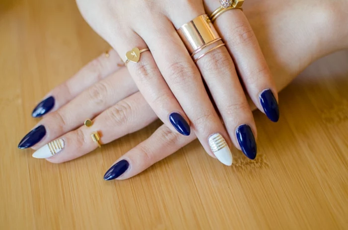 navy blue and white nail polish, on long oval nails, decorated with several thin, golden colored stripes, hands with several different golden rings