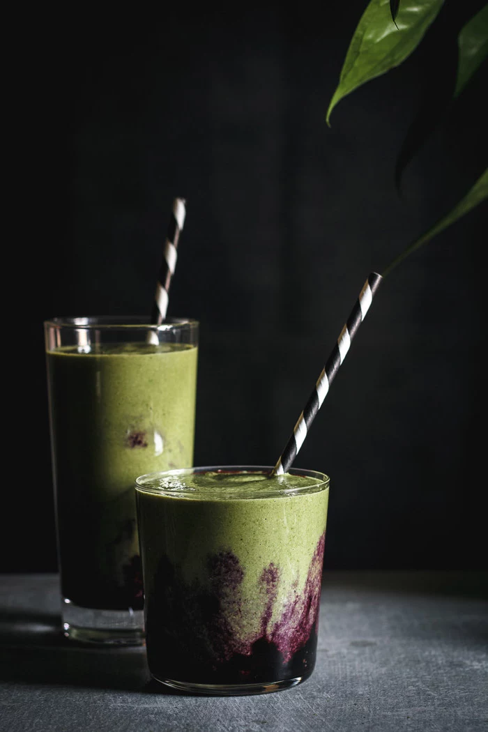 short and tall glasses, with striped straws, filled with blended dark purple, and light green mix, green smoothie recipe 