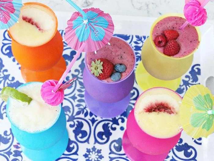 how to make a fruit smoothie, six plastic cocktail glasses, in different colors, filled with blended drinks, topped with different fruit, and paper umbrellas