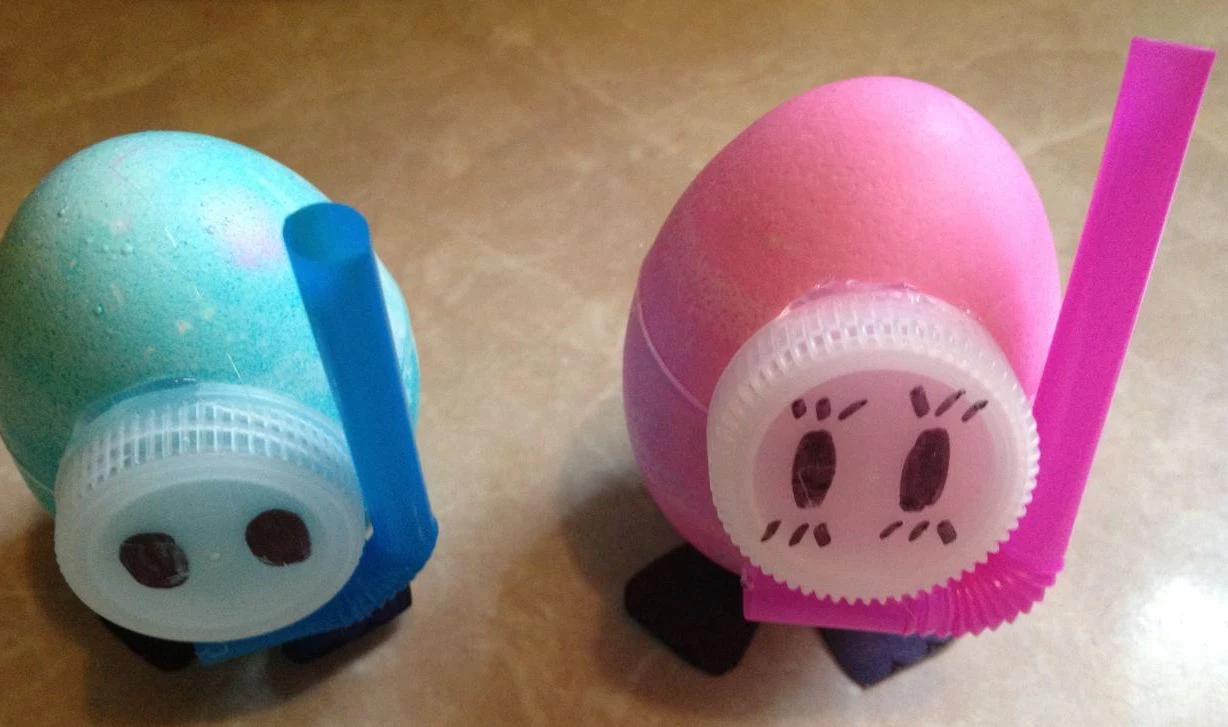 dyed eggs in pale pink, and light turquoise, decorated with sheer, plastic bottle caps, and bendy straws, easter crafts for preschoolers, made to look like snorkeling divers