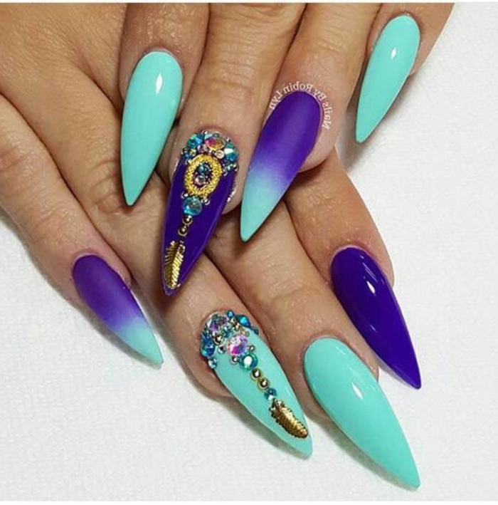 blue-green and purple claw nails, with ombre effect, various golden details, and many multicolored, gem-shaped nail decal stickers