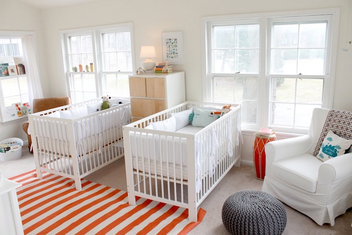 nursery ideas for twins, orange and white striped rug, pale beige carpet, two identical white, wooden cribs with cushions and toys