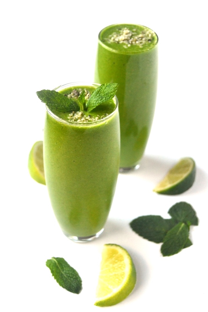 lime edges and mint leaves, near two tall glasses, filled with a green smoothie, each topped with small seeds