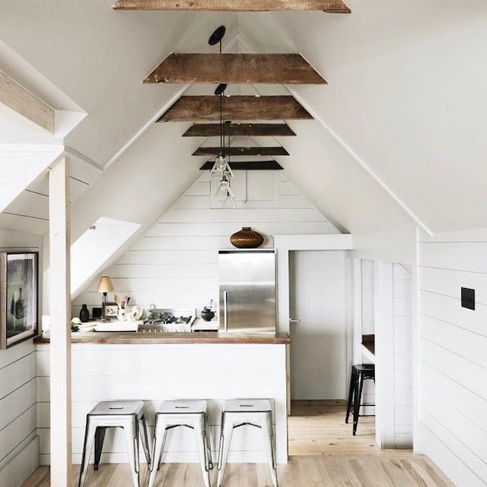 three shabby chic stools, near a kitchen counter, inside a room with light laminate floor, metal fridge and white vaulted ceiling, with brown beams