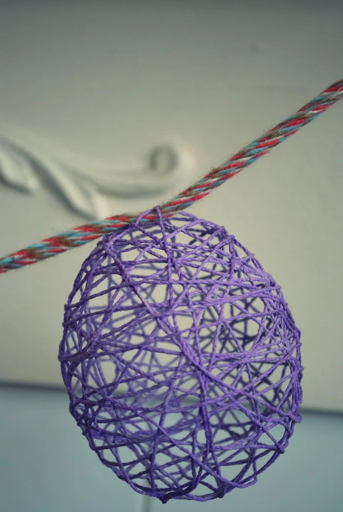 close up of a purple, meshy and hollow egg-shaped ornament, easter arts and crafts, hanging on multicolored woven rope