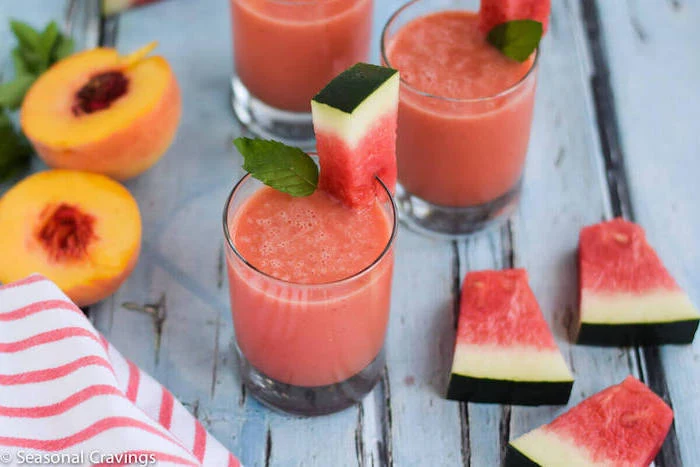 peach cut in two, near three glasses, filled with a blended watermelon drink, easy smoothie recipes, decorated with watermelon slices