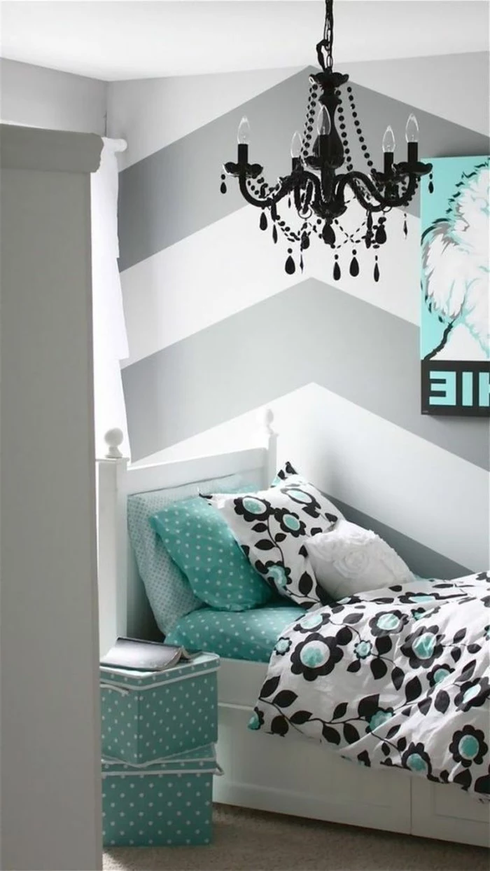 floral motives in black and teal, on white bed with teal bedding and pillow, striped walls in white and grey bedroom, ornate black baroque-style chandelier 