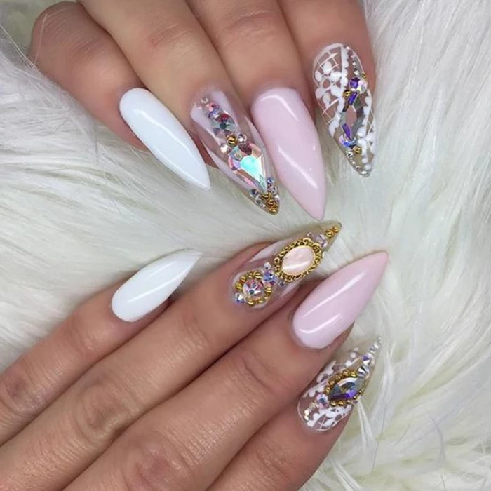 golden decorations and rhinestone stickers, on long pointy nails, painted in clear, white and pale pink nail polish