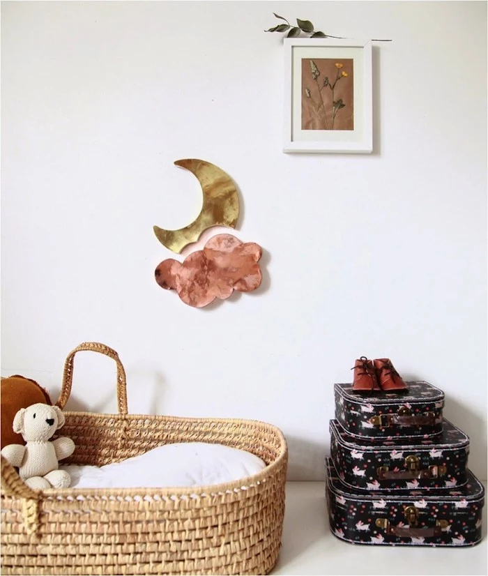 moon and pink cloud wall decoration, near wicker baby basket, three small decorative suitcases, framed dried flowers, baby girl nursery ideas