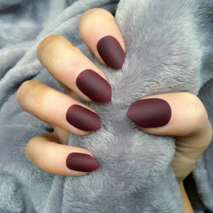 burgundy or deep red short stiletto nails, with sharp tips, on hand holding pale, grey plush blanket