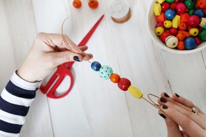 two hands with dark nail polish, holding piece of leather string, with five wooden beads, in different shapes and sizes, mother's day gift ideas 