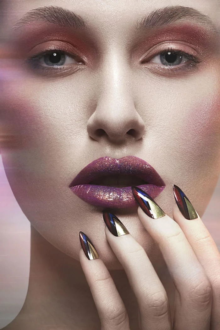 model with strong make-up, holding one hand to her face, with long manicure, stilleto nail designs, blue and black, red and gold metallic nail polish colors