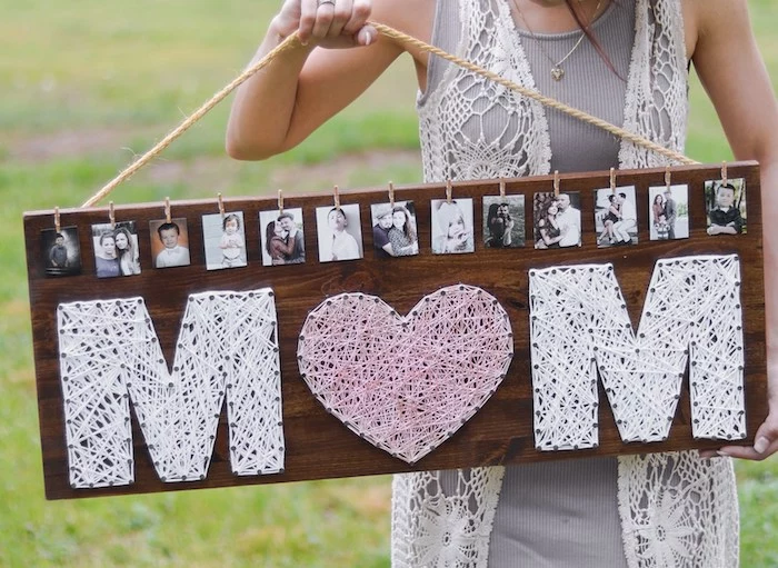 large board made of wood, decorated with photos, and the word mom, written in large letters, using thread and nails, top 10 mother's day gift ideas, rope handle held by slim woman