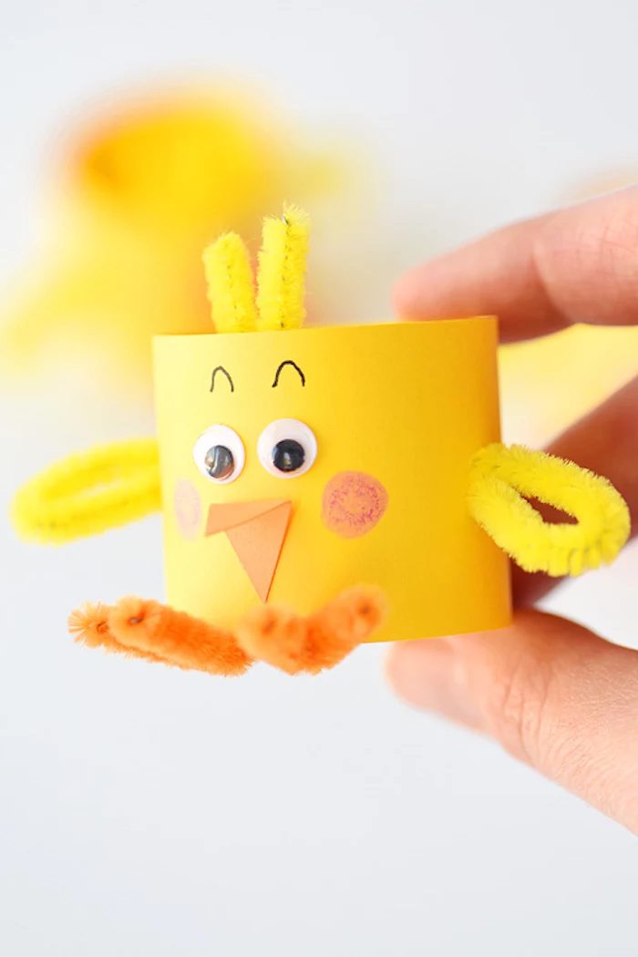 fuzzy wire in yellow and orange, stuck to small, yellow paper tube, decorated to look like a chick, held in a person's hand