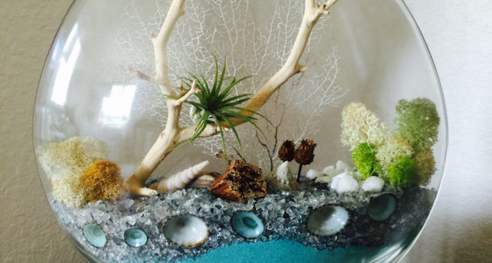 ivory white dried branch, with a small green tillandsia, inside a glass sphere, with turquoise sand, pale gray pebbles, and moss in different colors