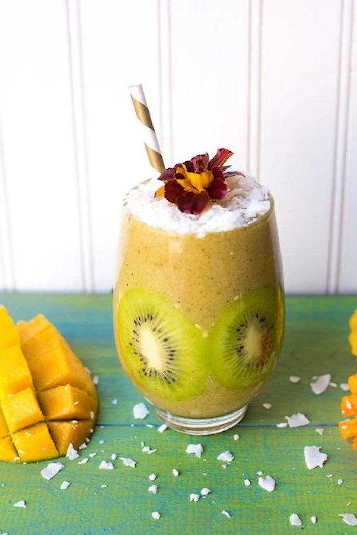 mango and kiwi blended drink, decorated with kiwi slices, easy smoothie recipes, topped with coconut flakes, and a red and yellow flower