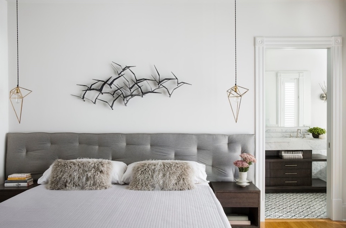 flock of black birds, 3D decoration mounted on a white wall, near modern hanging lamps, double bed with soft gray headboard, and two fluffy beige cushions