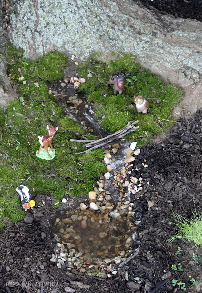 plastic animal figurines, Bambi and his friends, placed on green moss, near artificially made miniature stream, with pebbles and a tiny bridge, made of sticks, fairy garden images