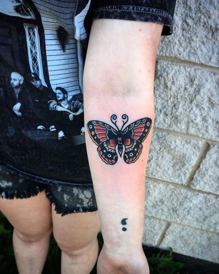 dark butterfly tattoo, with bold outlines, decorated with red, yellow and white, near a black semicolon tattoo, what does a semicolon tattoo mean, arm and wrist tattoos