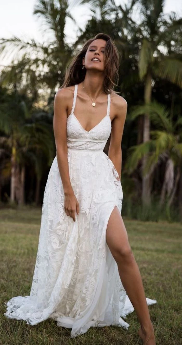 casual beach wedding dresses, young brunette woman, wearing an embroidered white maxi dress, with side slit, revealing her bare leg
