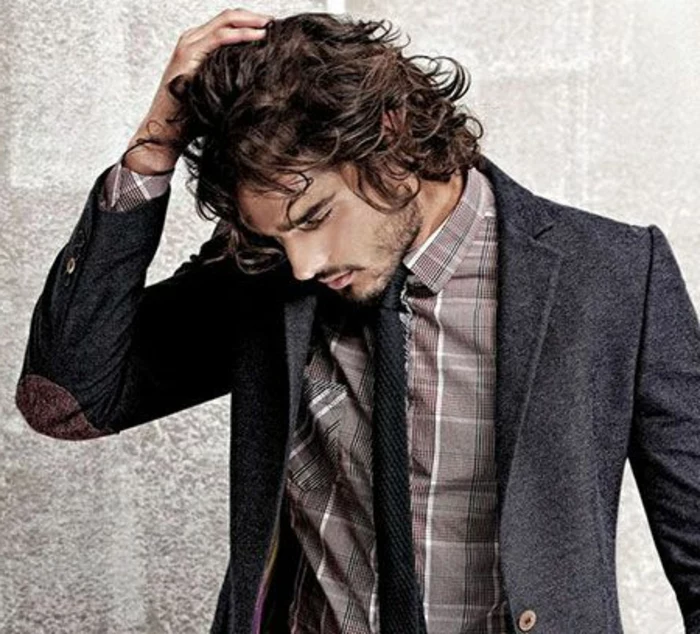 guys with curly hair, brunette man with tousled hair, wearing dark grey blazer, with elbow patches, over brown plaid shirt, stubble and mustache