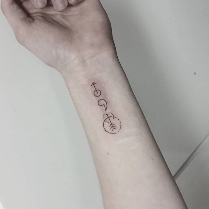 semicolon tattoo meaning, pale white hand, with minimalistic black wrist tattoo, featuring a semicolon, arrows and circles