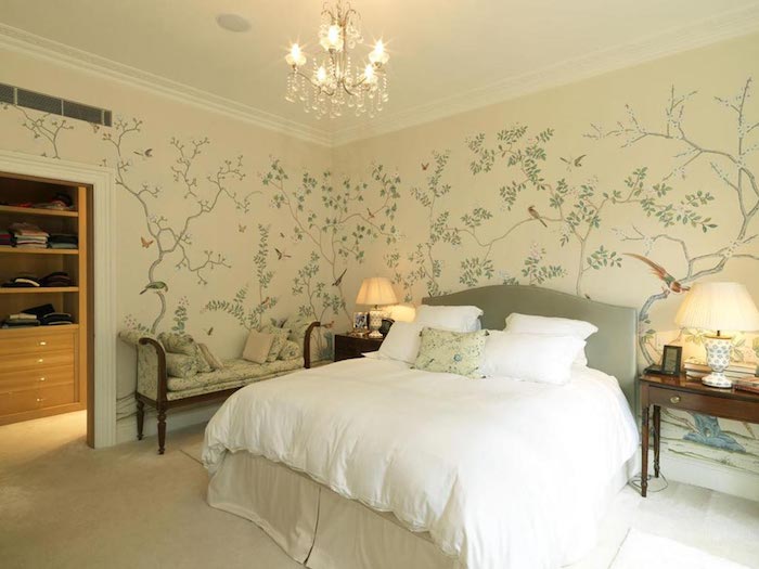 delicate botanical wallpaper, in cream and pale green, with thin trees and different birds, decorating the walls of a bedroom, with large fluffy bed