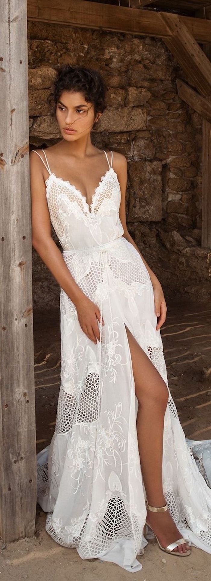 maxi dress in white, with lace inserts and embroidery, featuring thin straps and a slit, casual beach wedding dresses, worn by tanned brunette young woman, with curly dark hair put up, and silver heeled sandals